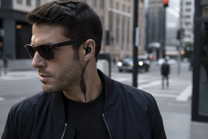 Man wearing sunglasses and black earbuds in an urban setting with SIlynx VIP Covert Headset.