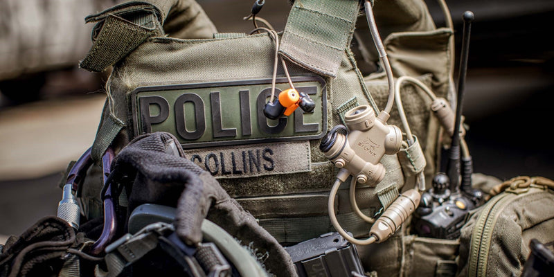 Close-up of a police officer's tactical gear with Silynx Clarus headsets and  visible 'POLICE' insignia.