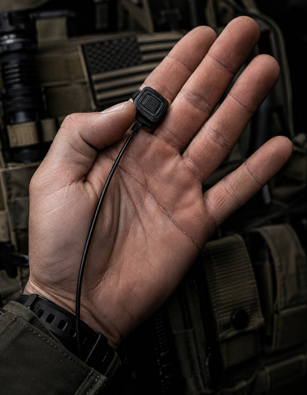Silynx finger PTT tactical device on a person's palm with military background