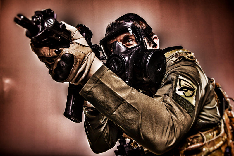 Person in military gear with a gas mask Silynx Earpiece and weapon on a brown background