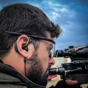 Soldier using Silynx Protego headset with a rifle and a scope and ear protection against a cloudy sky.