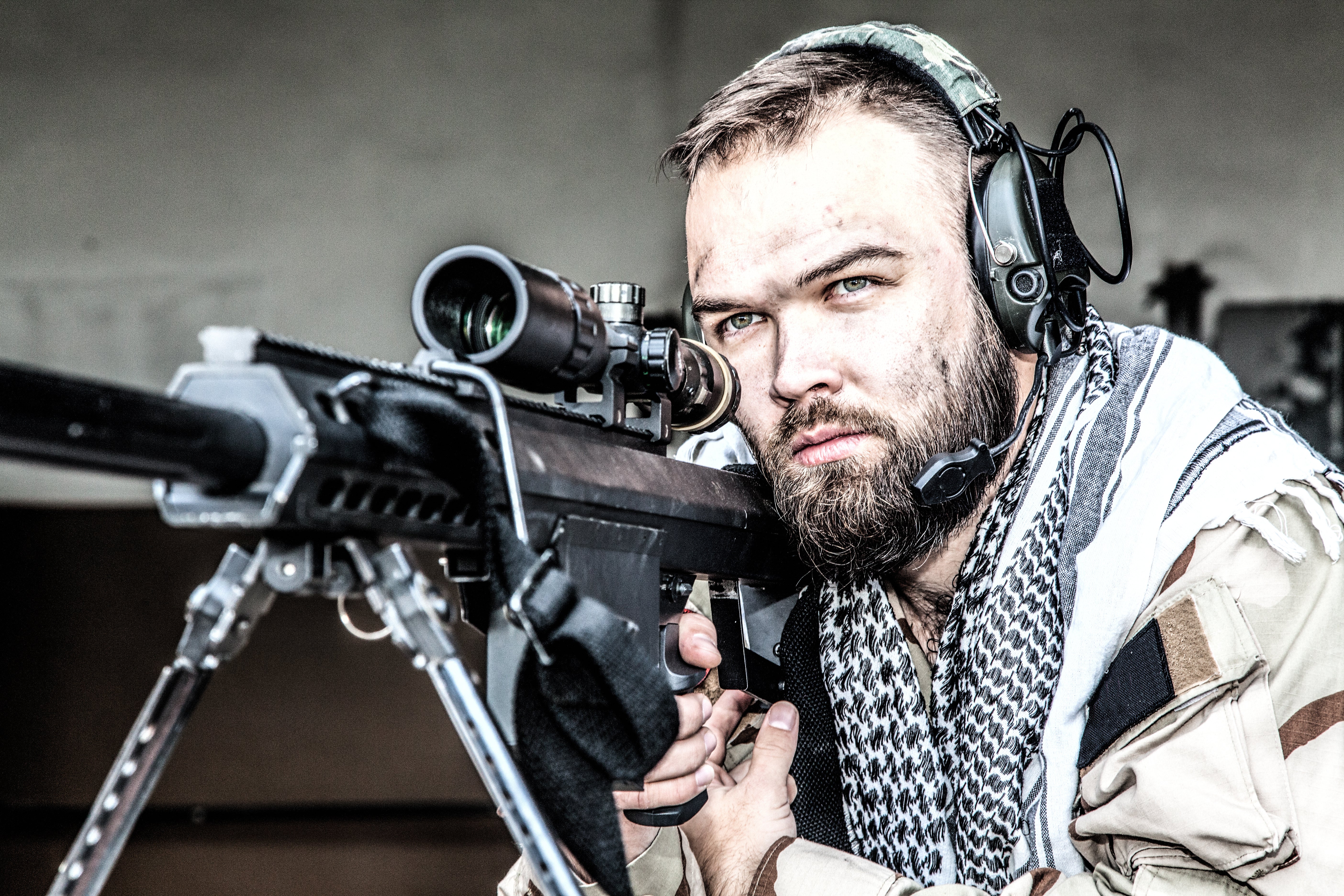Man with a beard holding a rifle with a scope, wearing Silynx Protego SDR and a scarf.