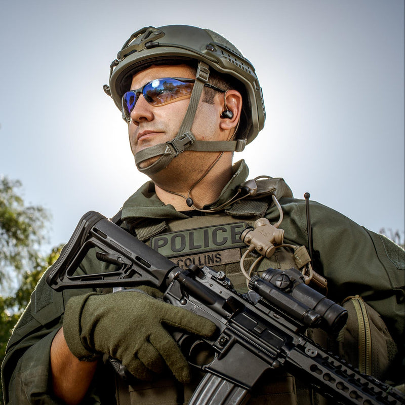 Police Law Enforcement with Clarus Headset system in tactical gear holding a firearm with trees in the background